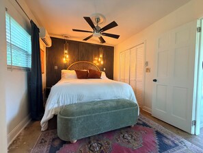 A bedroom with a bed, a ceiling fan, a window with blinds, a door, and a patterned rug. - Blissful Marsh Front GuestHouse Getaway! (Charleston)