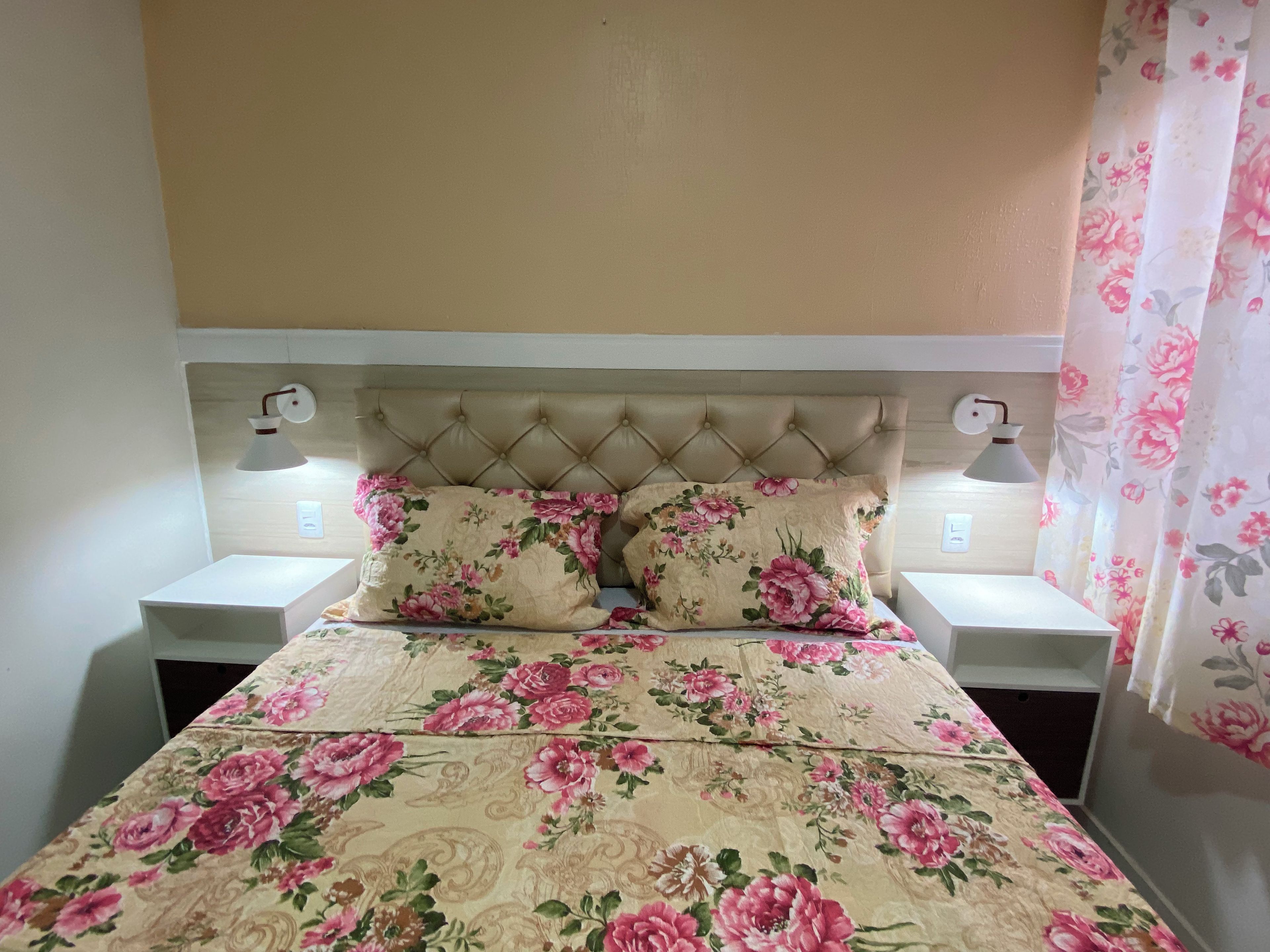 A bed with a floral bedspread, two pillows, a tufted headboard, and bedside lamps.