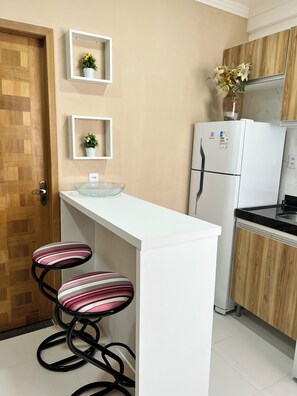 A kitchen with a white countertop, two striped bar stools, a refrigerator, and two wall-mounted shelves with potted plants. - 102 Acolhedor e aconchegante (Belém)