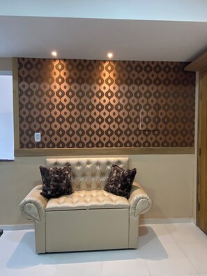 A room with a patterned wall, a tufted sofa with cushions, and a tiled floor. - 102 Acolhedor e aconchegante (Belém)