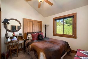 Ein Schlafzimmer mit Bett, Schreibtisch, Stuhl, Fenster und Deckenventilator.