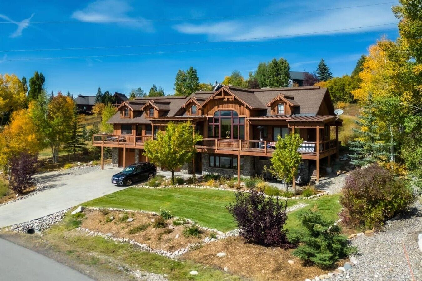 A large, two-story wooden cabin with a covered porch and a car parked in front.