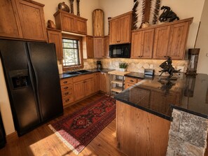 A kitchen with wooden cabinets, a black refrigerator, a microwave, and a decorative rug. - Dallas Chalet | 7BD 4.5BA with Hot Tub and Views! (Steamboat Springs)