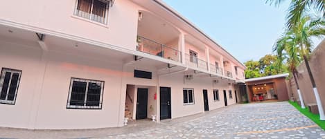 A building with a flat facade, multiple windows with metal bars, a balcony with a railing, and a tiled ground floor.