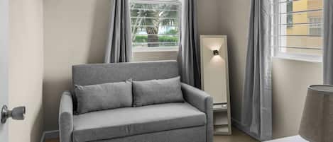 A neutral-toned room with a grey sofa, a standing floor lamp, and a window with curtains.