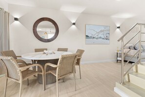 A modern dining area with a round table surrounded by wicker chairs, a large mirror on the wall, and a painting depicting a beach scene. - Stylish, Comfortable, Private townhouse steps to Dover Beach & St. Lawrence Gap (Oistins)