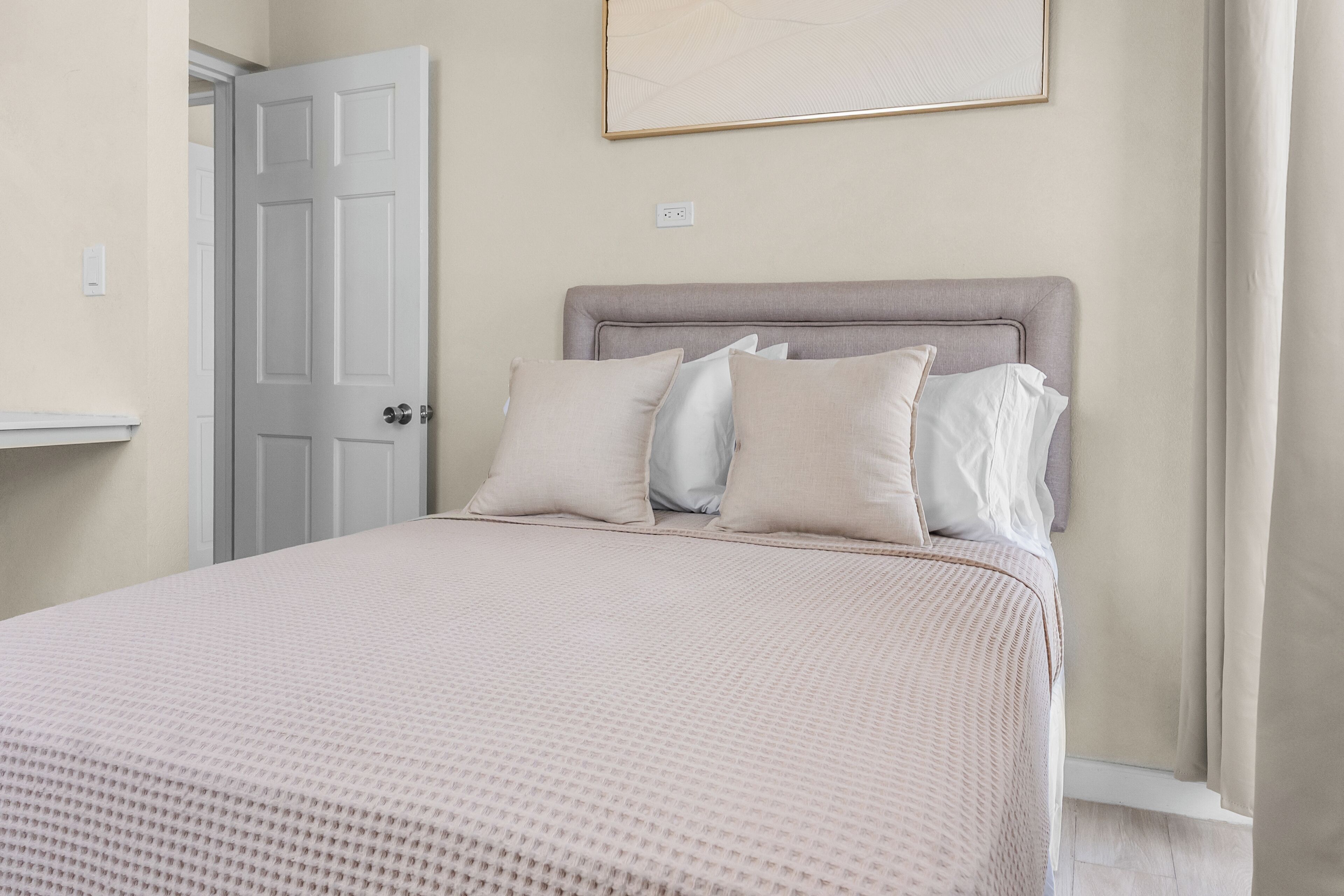 Un dormitorio con cama, almohadas, cabecero, una puerta y un aplique de pared.