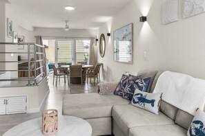 A modern living room with a sectional sofa, a dining area with wicker chairs, and a kitchen area with a glass railing. - Stylish, Comfortable, Private townhouse steps to Dover Beach & St. Lawrence Gap (Oistins)