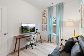A modern living room with a wooden desk, a television, a sofa, and a window with curtains. - BRING THE WHOLE CREW ★ 5BR HOME, SLEEPS 16 + HOT TUB, GAMES & BBQ (Charlotte)