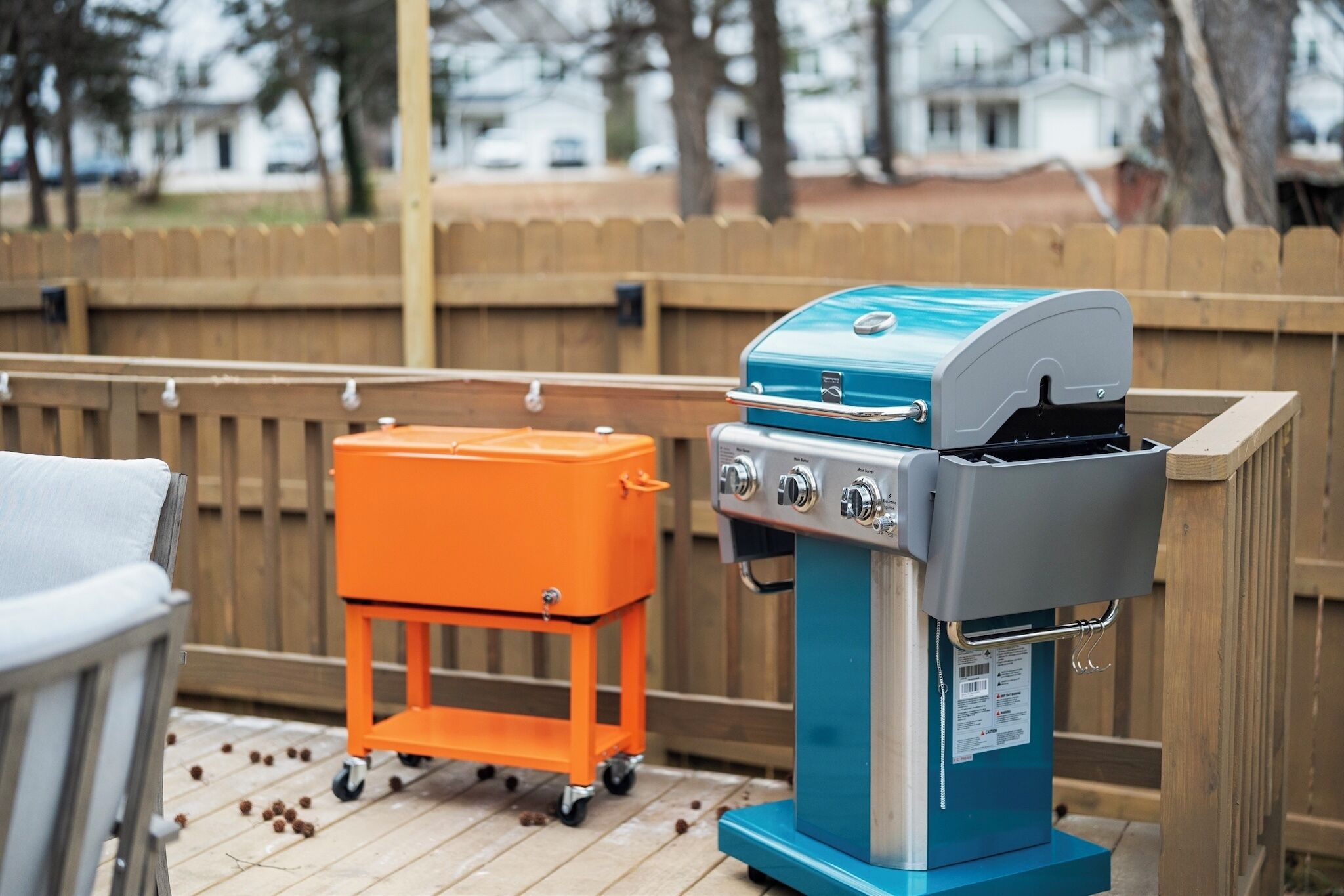 A barbecue grill with a side cart and a grill cover on a wooden deck.
