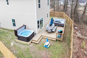 A backyard with a hot tub, outdoor seating, and a wooden deck. - BRING THE WHOLE CREW ★ 5BR HOME, SLEEPS 16 + HOT TUB, GAMES & BBQ (Charlotte)