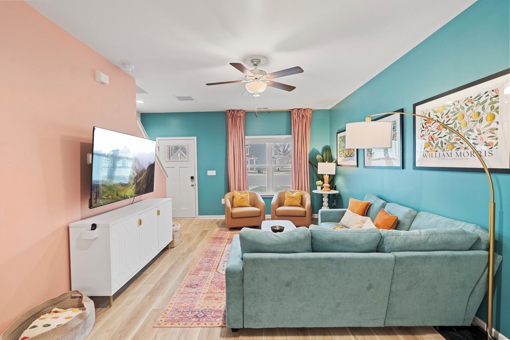 Un salon avec un canapé de couleur turquoise, deux fauteuils, un téléviseur et un ventilateur de plafond.