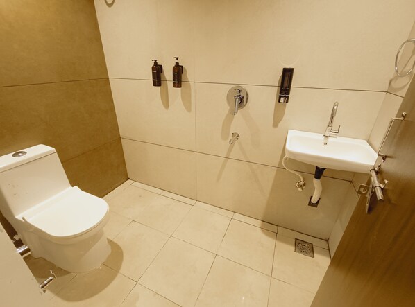 Un baño con inodoro, lavamanos y dos secamanos fijos en la pared.