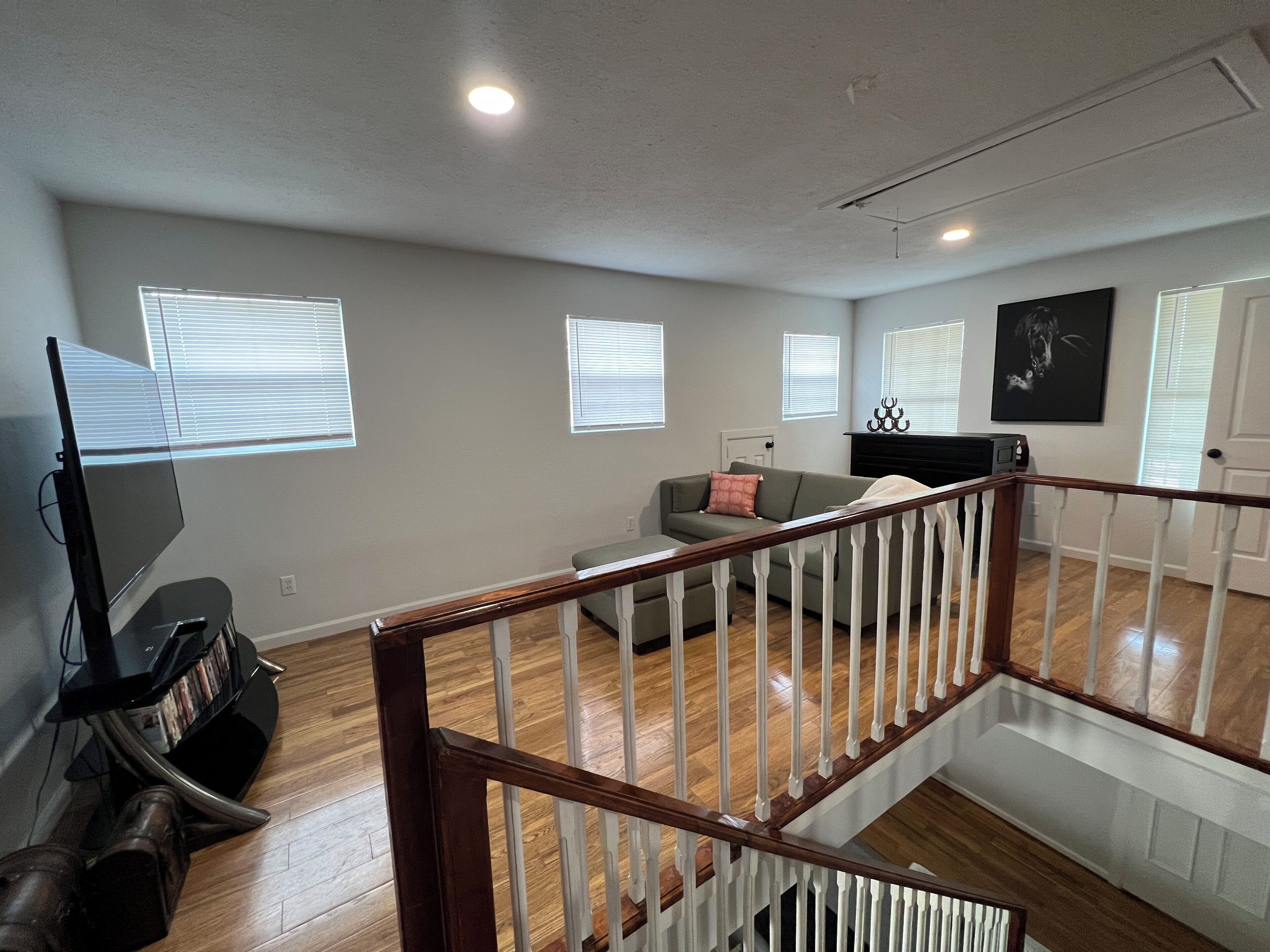 A spacious living area with a wooden staircase, a grey sofa, and a television.