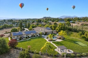A residential area with a large house featuring a solar panel roof, a swimming pool, and a well-maintained lawn. - Wine Country Estate w/ Pool, Spa, Theater & Golf (Temecula)
