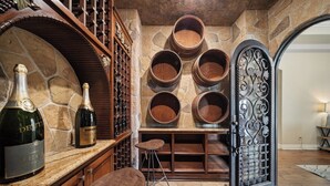 A wine cellar with wooden barrels, a wine rack, and a bar area with stools. - Wine Country Estate w/ Pool, Spa, Theater & Golf (Temecula)