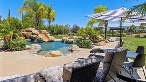 A pool area with lounge chairs and a table, surrounded by rocks and palm trees. - Wine Country Estate w/ Pool, Spa, Theater & Golf (Temecula)