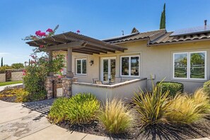 A residential house with a pergola, a stone wall, and a variety of plants.