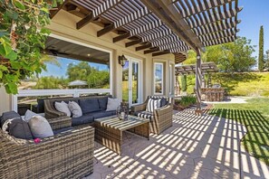Un patio al aire libre con mobiliario de mimbre, una pérgola y vistas del paisaje circundante.