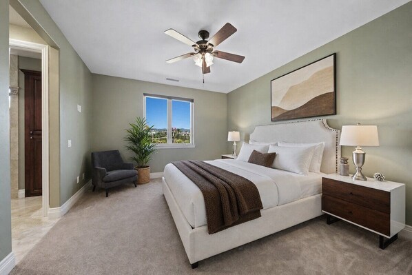A bedroom with a bed, bedside tables, a ceiling fan, a window, and a view of the outdoors.
