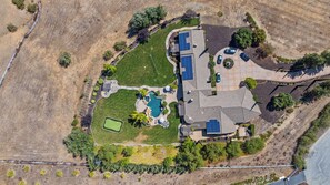 Vista aérea de una propiedad residencial con piscina, cancha de tenis y paneles solares.