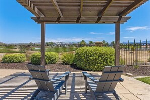 A covered outdoor seating area with benches and a pergola, surrounded by a fence and greenery.