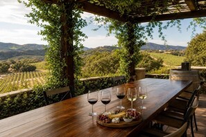 A wooden table set outdoors with wine glasses, cheese, and olives, overlooking a vineyard. - Wine Country Estate w/ Pool, Spa, Theater & Golf (Temecula)