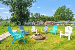 Ein Garten mit Feuerstelle, mehreren Adirondack-Stühlen und einer Holzterrasse.