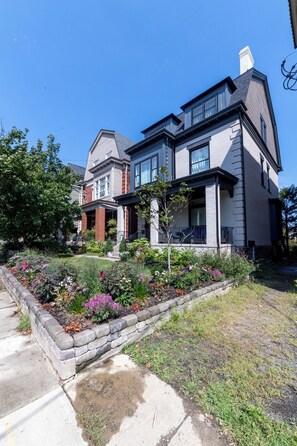 A two-story house with a front porch and a garden with various plants and flowers. - Luxury 5BR Shadyside Home Near CMU • Walk to Walnut St & Bakery Square (Pittsburgh)