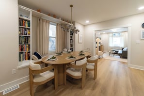 Een eethoek met een ronde tafel, zes stoelen en een boekenplank vol boeken.