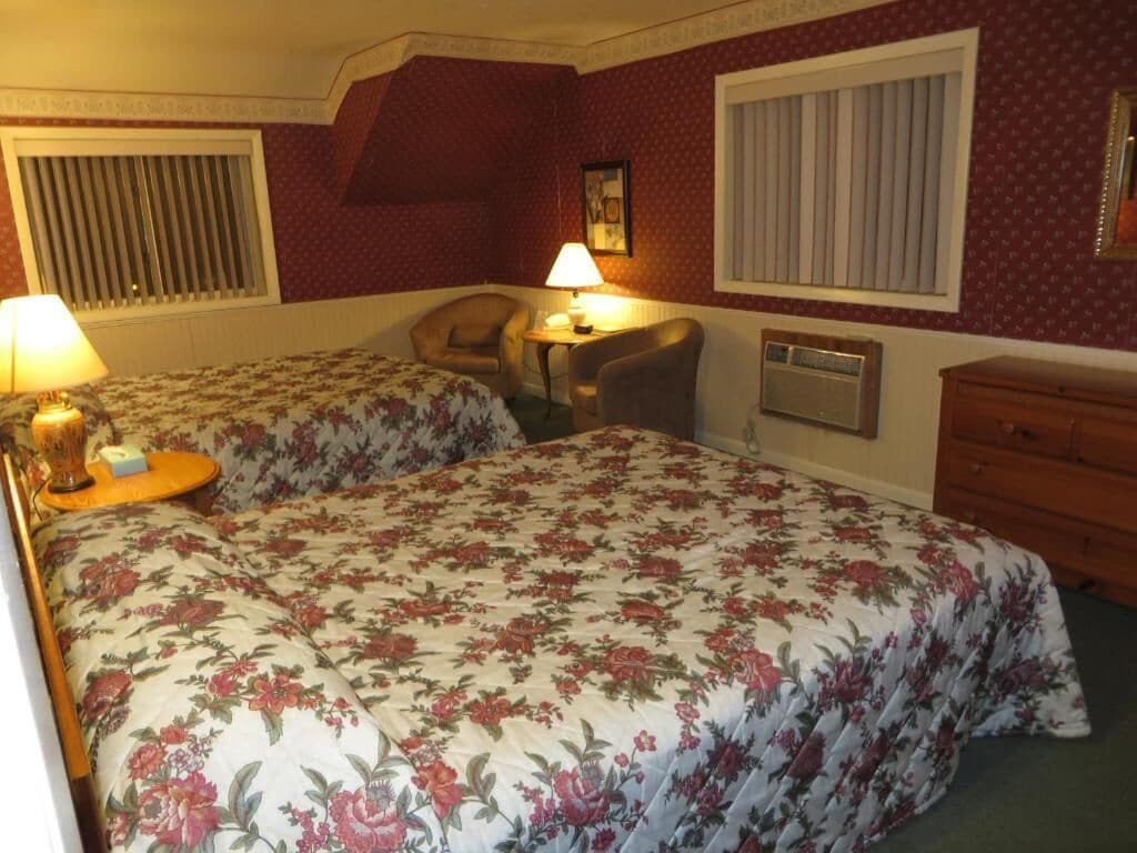 A hotel room with two beds, a desk, a chair, a dresser, and a window with blinds.