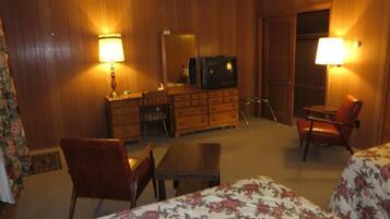 A hotel room with a bed, a desk, a chair, a dresser, and a television.