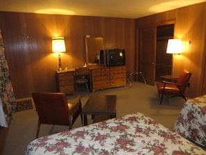Una habitación de hotel con una cama, un escritorio, una silla, un aparador y un televisor.