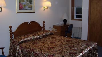 Ein Schlafzimmer mit einem hölzernen Bett, einem Nachttisch, einem Schreibtisch, einem Stuhl, einem Heizkörper und einem Fenster mit Jalousien.