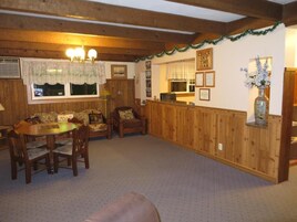 Una habitación con paneles de madera, una mesa de comedor con sillas, un sofá, un televisor y un jarrón decorativo.