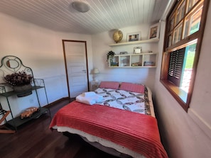 Ein Schlafzimmer mit einem Bett, einem Regal mit Büchern und einem Globus, einer Tür und einem Fenster mit Fensterläden.