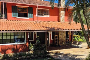 Un edificio rojo con techo de tejas, un patio cubierto con mobiliario exterior y un muro de piedra.