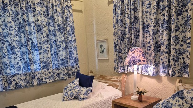 A room with two single beds, a wooden nightstand with a lamp, and floral curtains.
