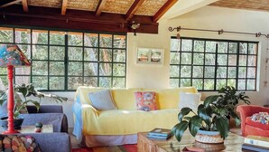 A cozy living room with a wooden ceiling, large windows, and a colorful striped rug.