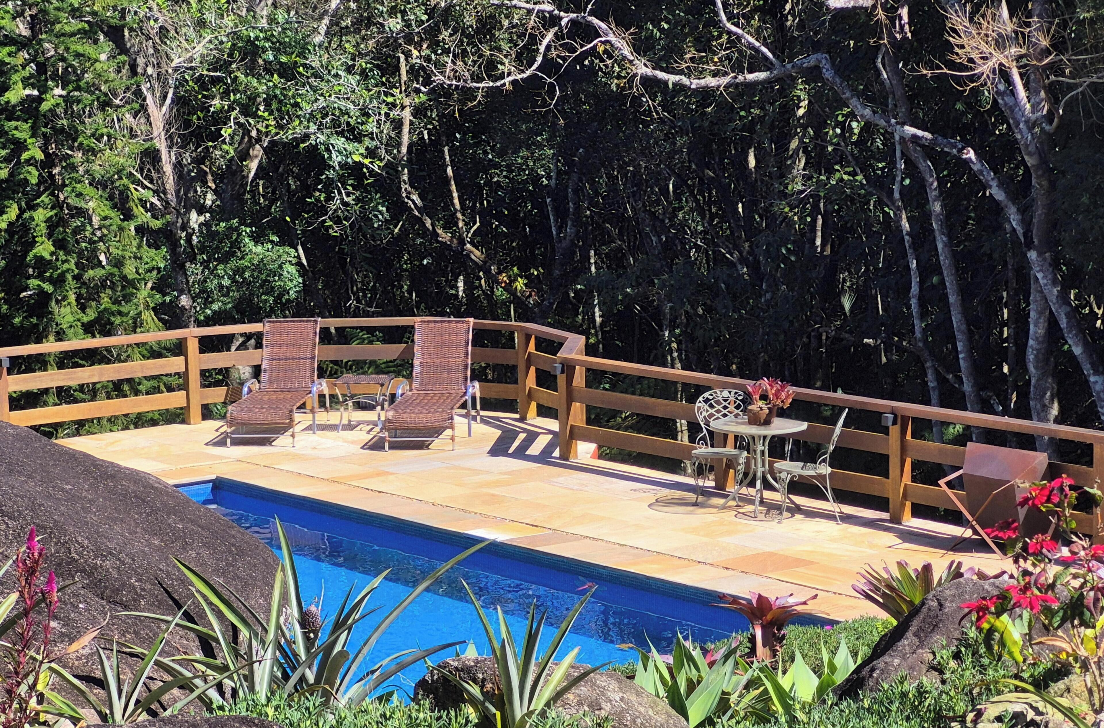 Een zwembadgedeelte met een houten terras, ligbedden en een tafel met stoelen.