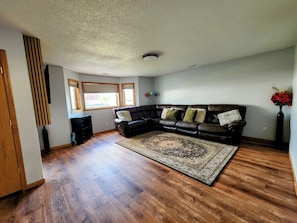 A living room with a sectional sofa, a patterned rug, and wooden flooring. - 3-bedroom house in peaceful Fargo with cool AC breeze (Fargo)