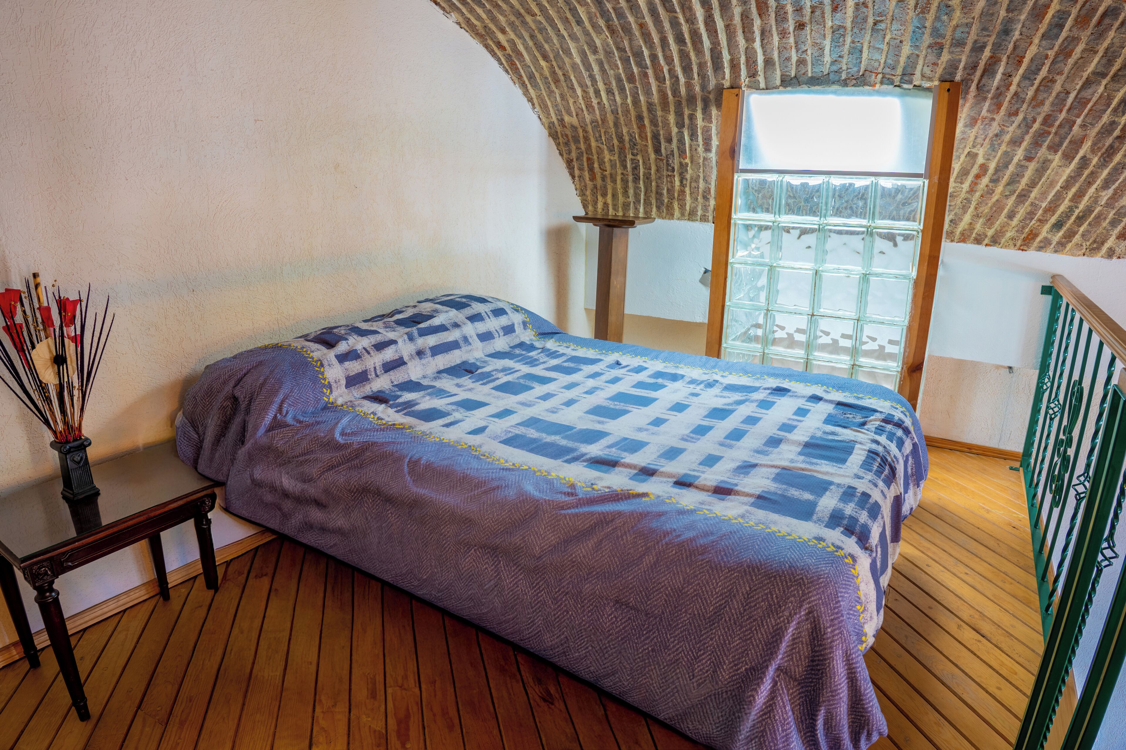 A room with a bed, a wooden floor, a window with a view, and a brick wall.