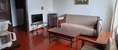 Una sala de estar con un sofá, una mesa de centro, un televisor sobre un mueble bajo, un refrigerador y una chimenea.