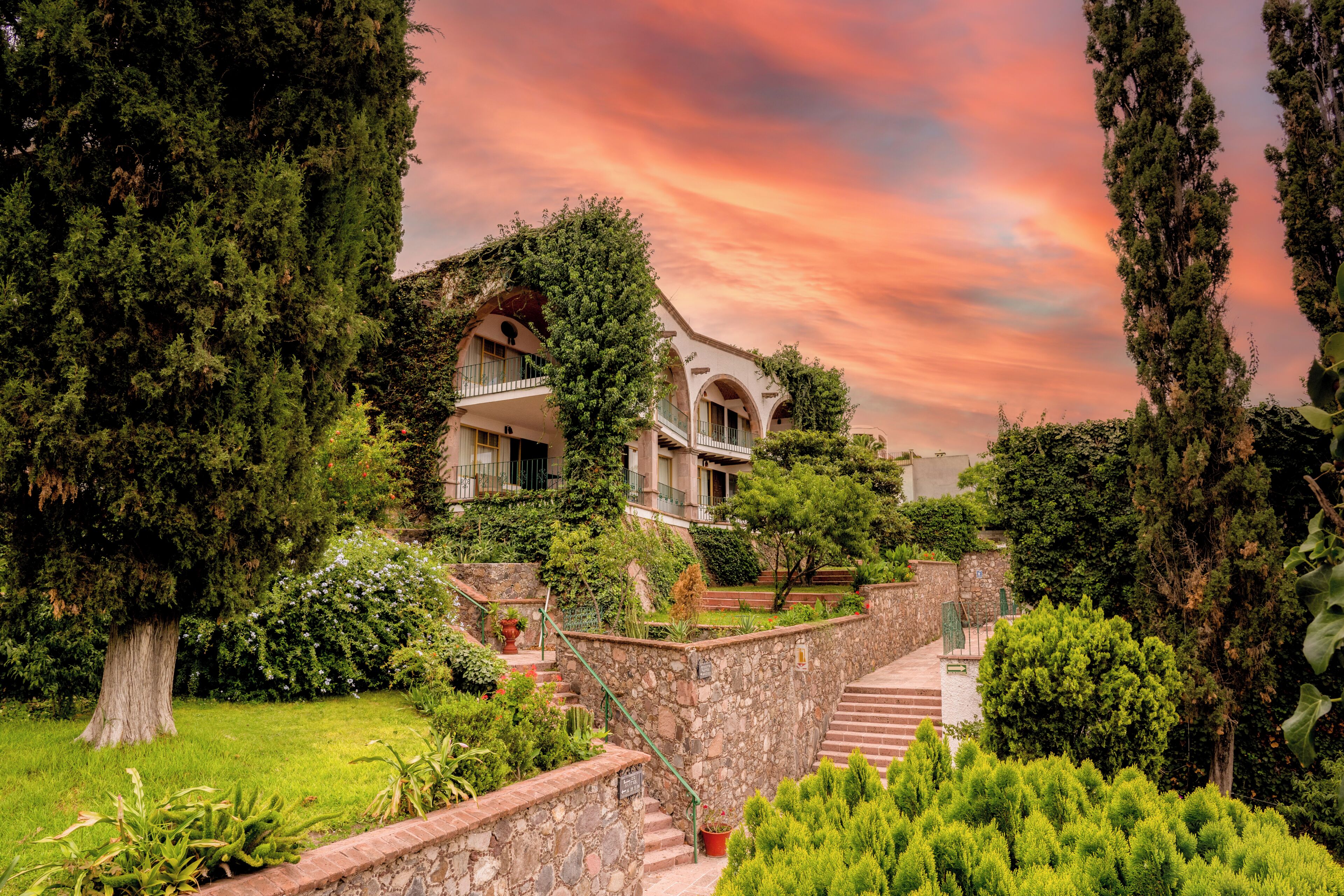 A building with a stone staircase leading to a balcony, surrounded by lush greenery and trees.