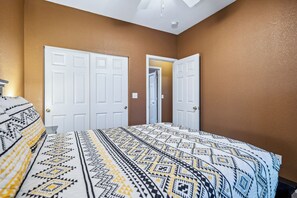A bedroom with a patterned bedspread, two white doors, and a brown wall. - Cozy desert home near the Laughlin River (Bullhead City)