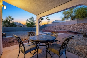 An outdoor patio with a round table and chairs, a pool, and a view of a residential area with palm trees and a brick wall. - Cozy desert home near the Laughlin River (Bullhead City)