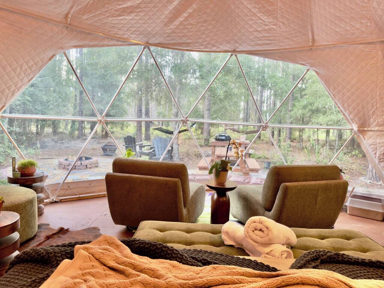 A tented accommodation with two sofas, a rug, and a view of a forested area.