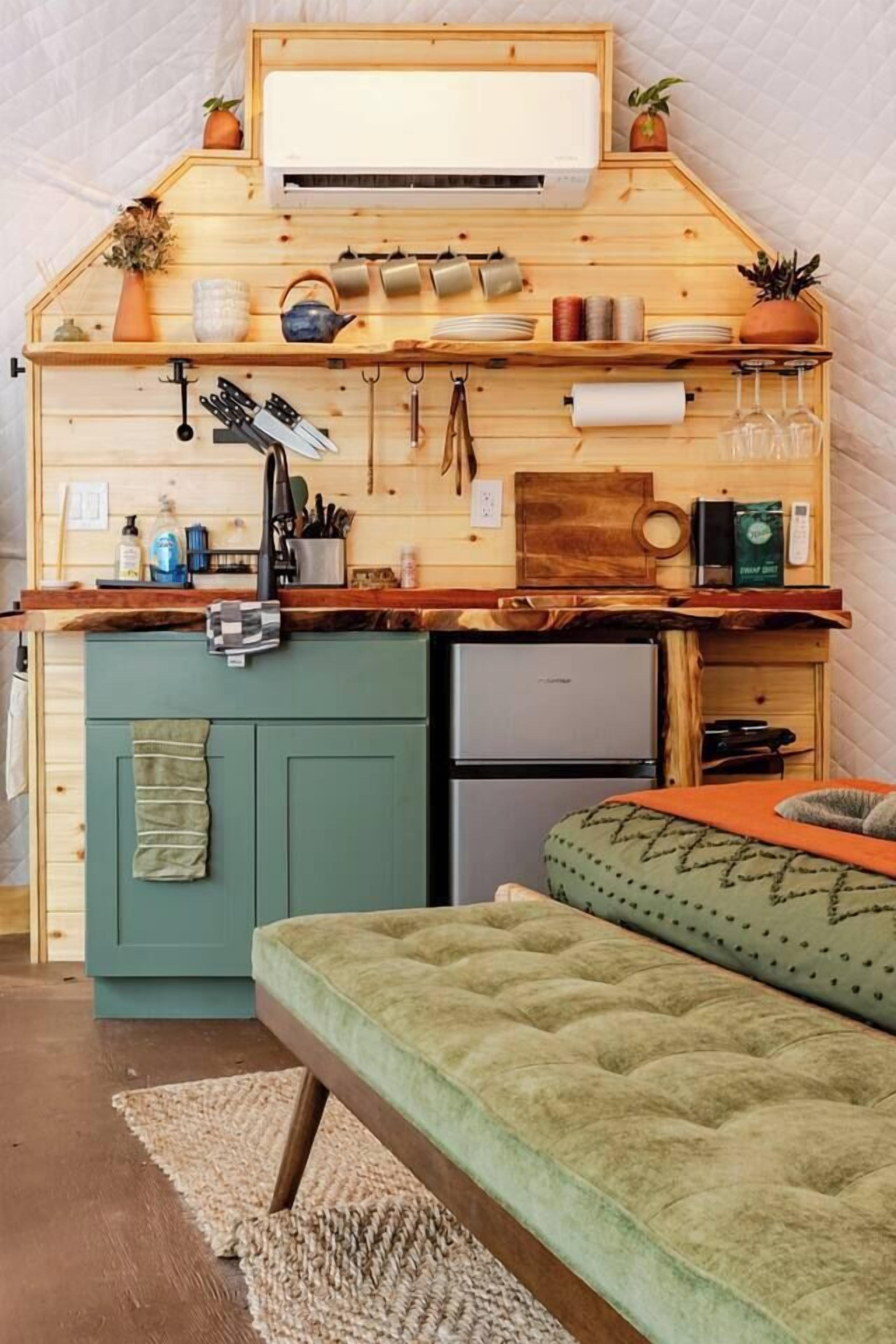 A compact kitchenette with a built-in refrigerator, a sink, and a countertop with various kitchen utensils and appliances.