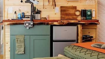 A compact kitchenette with a built-in refrigerator, a sink, and a countertop with various kitchen utensils and appliances.