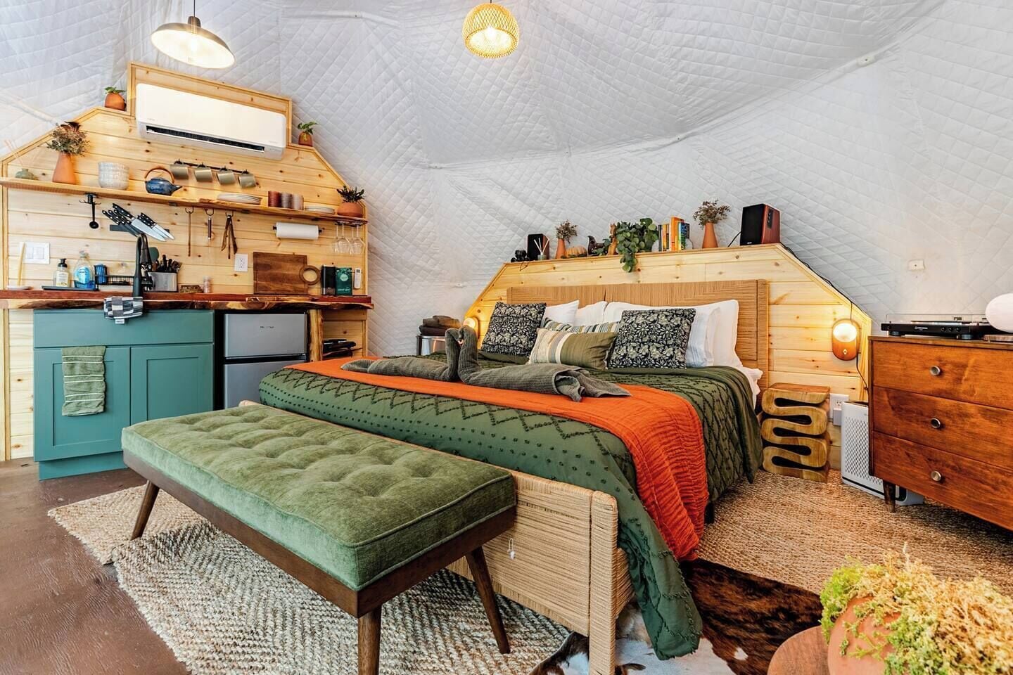 A cozy tent-style accommodation with a kitchenette, a bed with multiple pillows, and a bench.